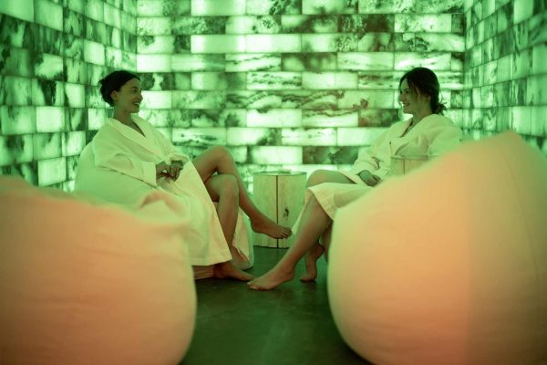 two women in bathrobe relaxing in salt room with green light