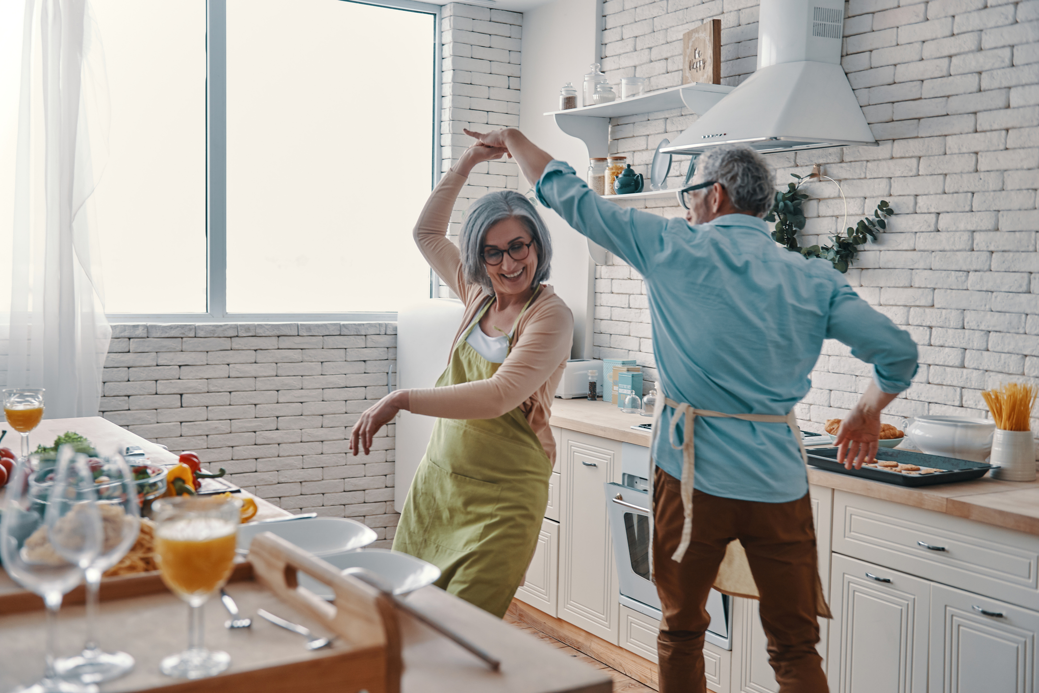 Beautiful playful senior couple in aprons dancing and smiling while preparing healthy dinner at home